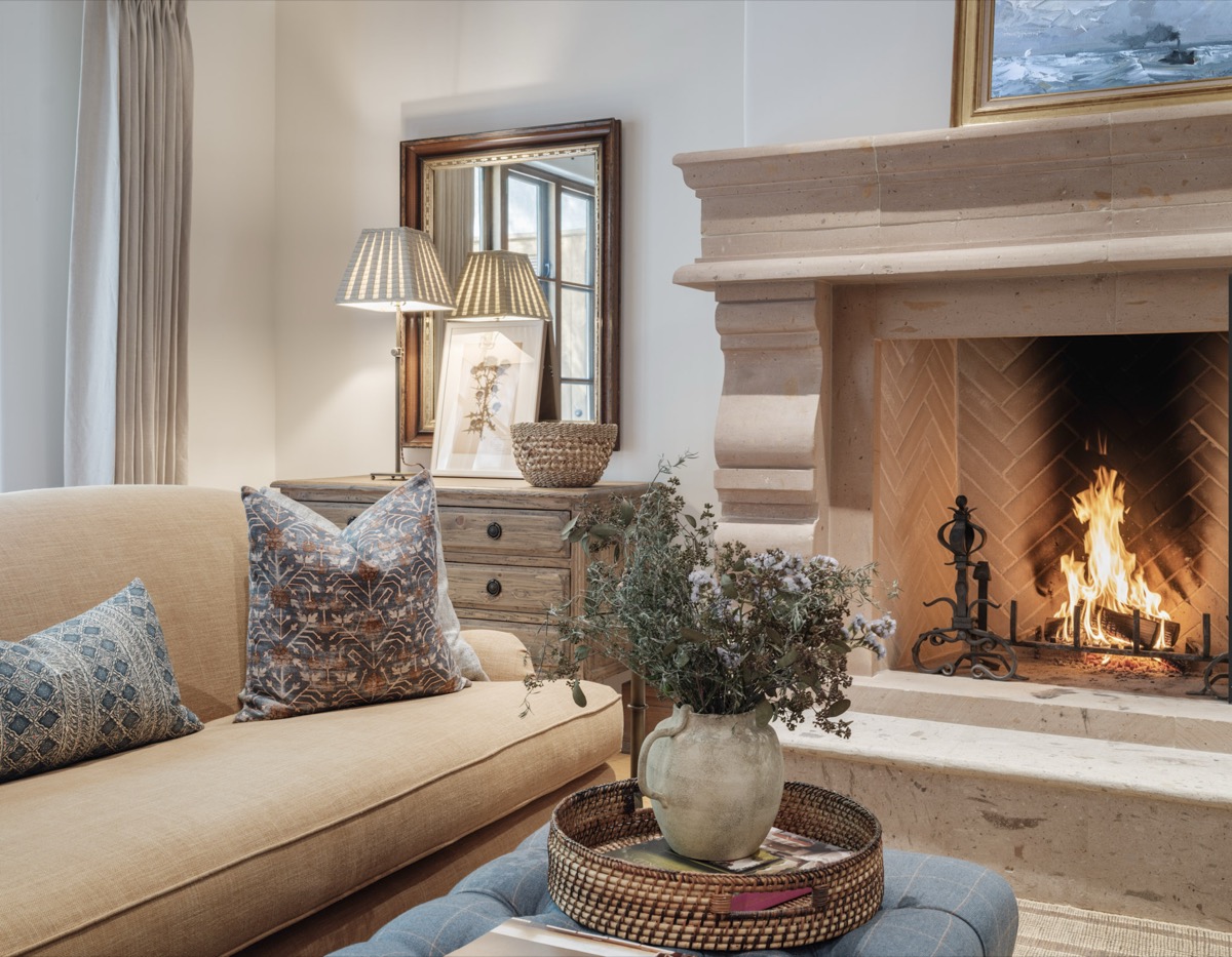 Living room with a stone fireplace, neutral sofa and woven ottoman