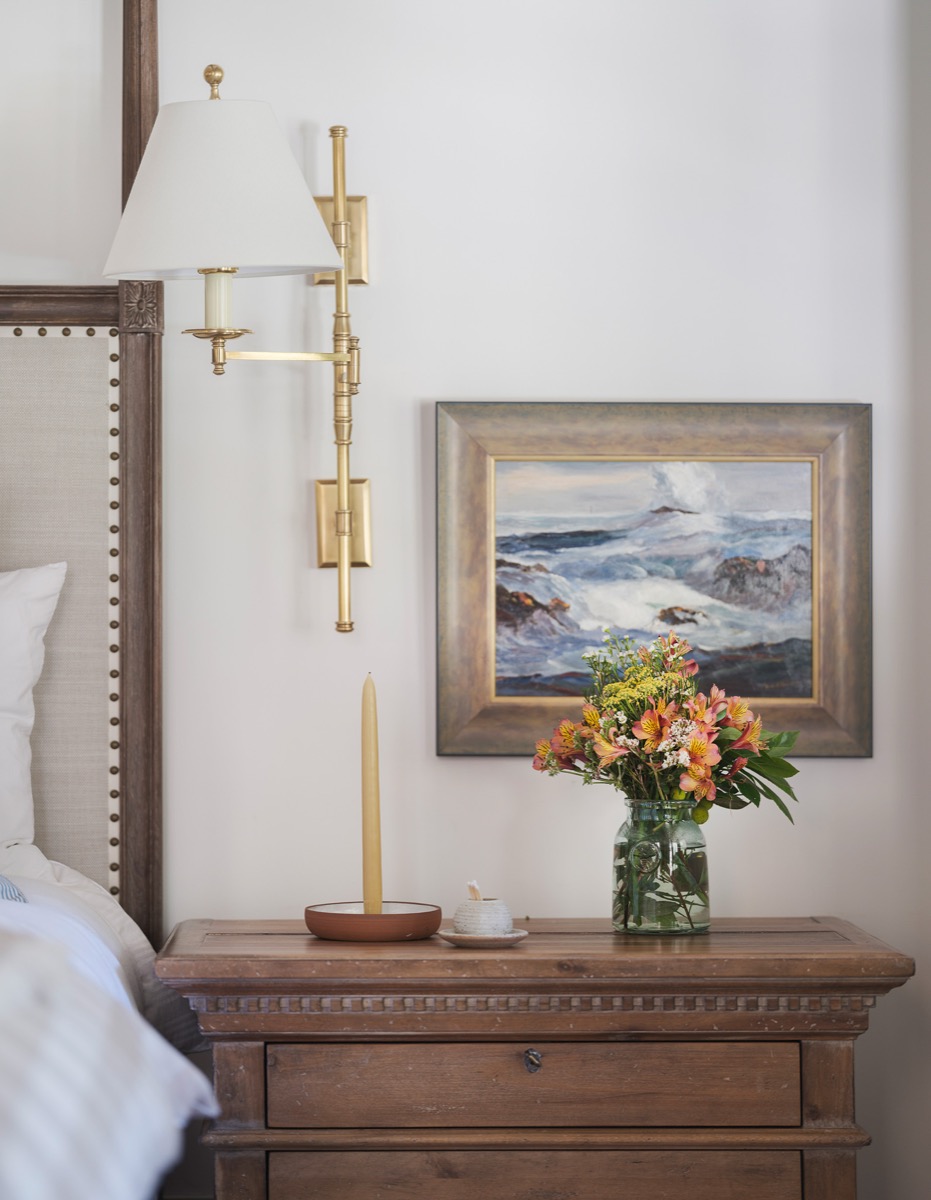 Bedside vignette with a brass sconce and framed coastal artwork